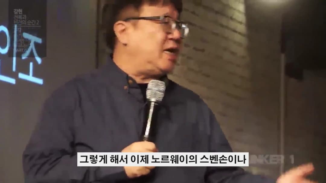 안경을 쓴 중년 남성이 마이크를 들고 강연하는 모습