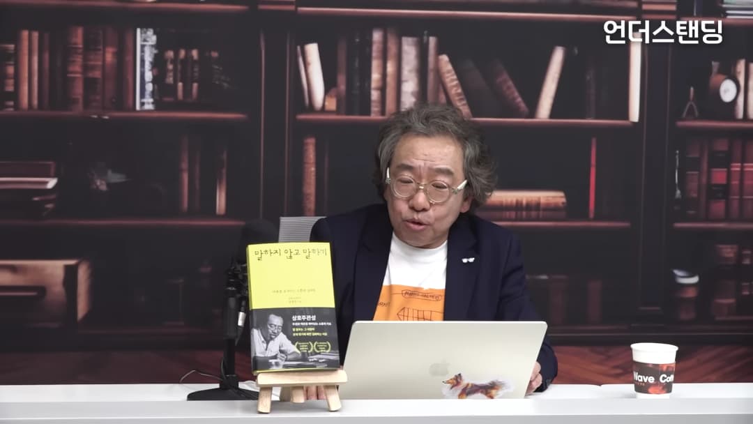 서재 배경의 스튜디오에서 책을 앞에 두고 이야기하는 중년 남성