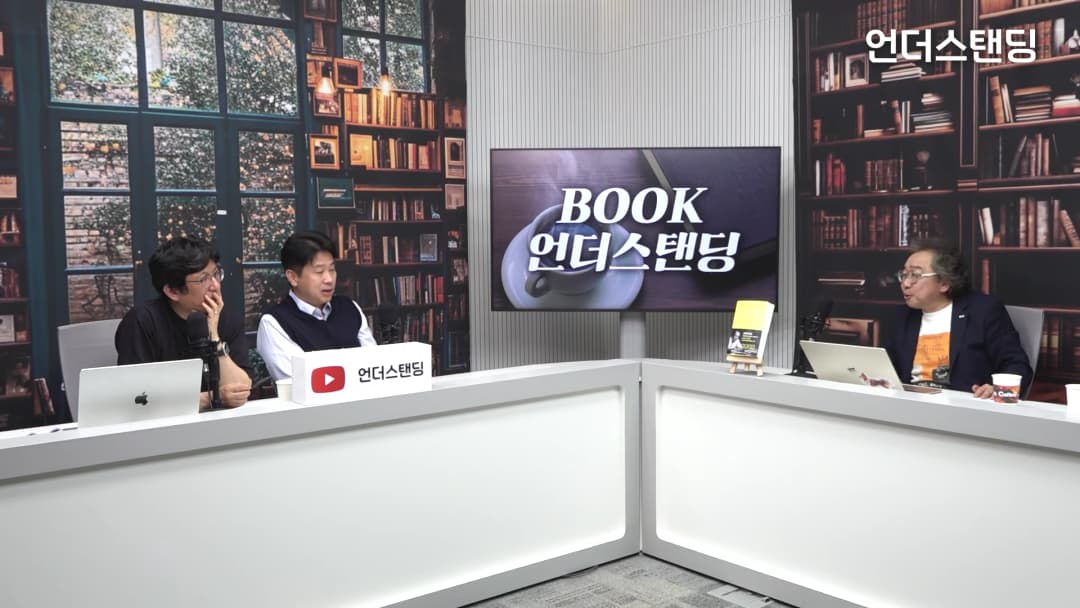 서재 배경의 스튜디오에서 세 명의 남성이 테이블에 앉아 대화를 나누고 있다.