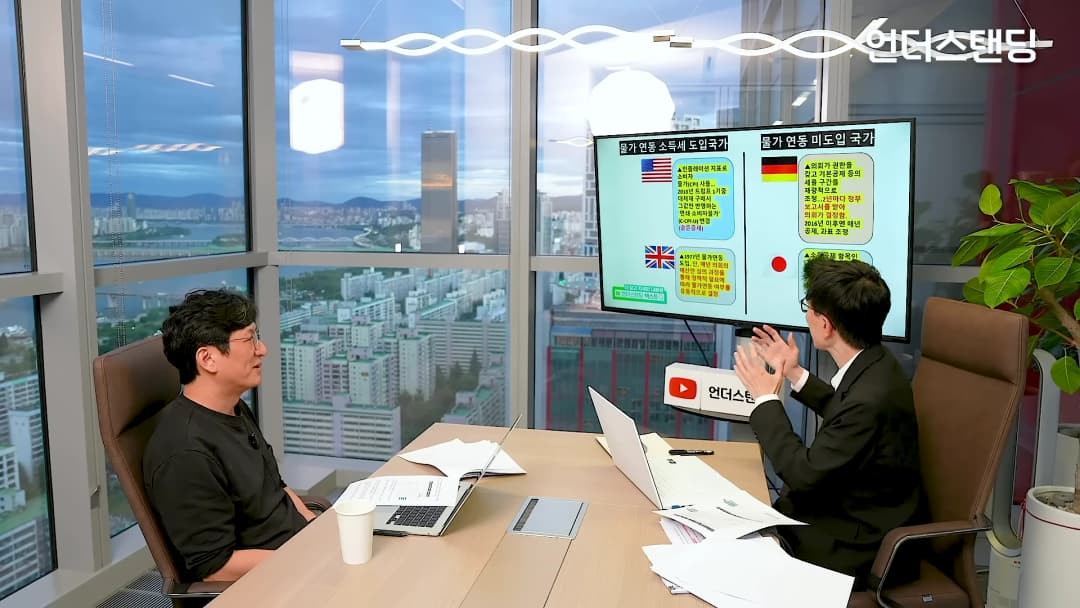스튜디오에서 두 남성이 대화하며 물가 연동 소득세 도입 국가와 미도입 국가를 비교한 화면을 보고 있다.