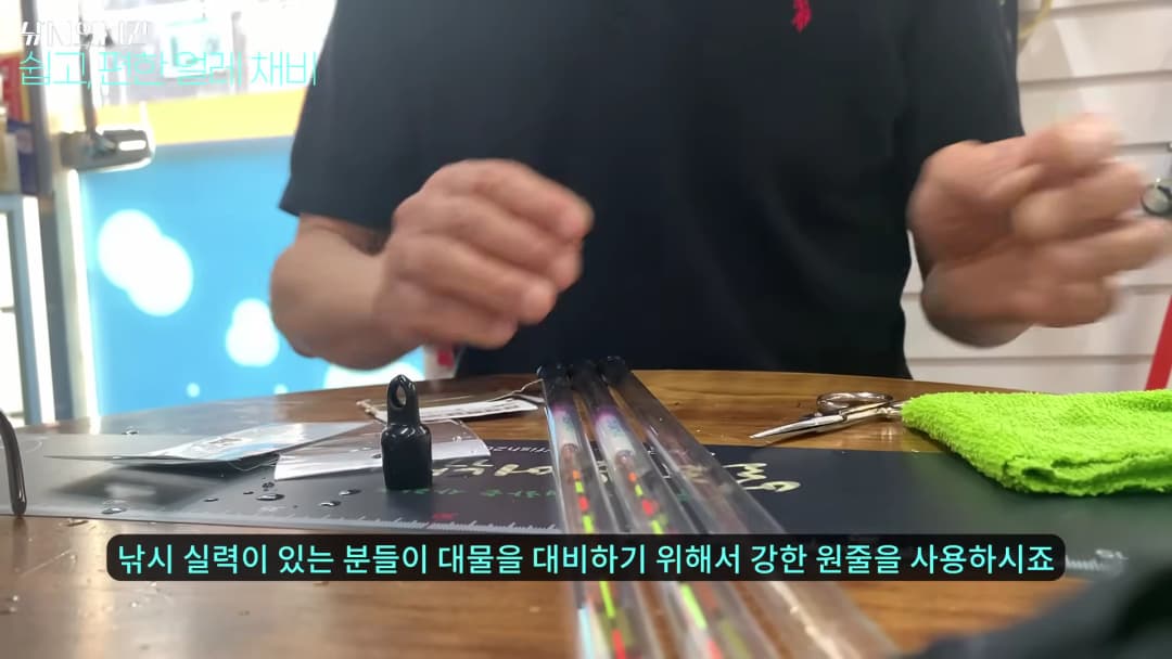낚시 전문가가 테이블 위에 놓인 찌와 낚시 도구들을 손으로 가리키며 설명하는 모습