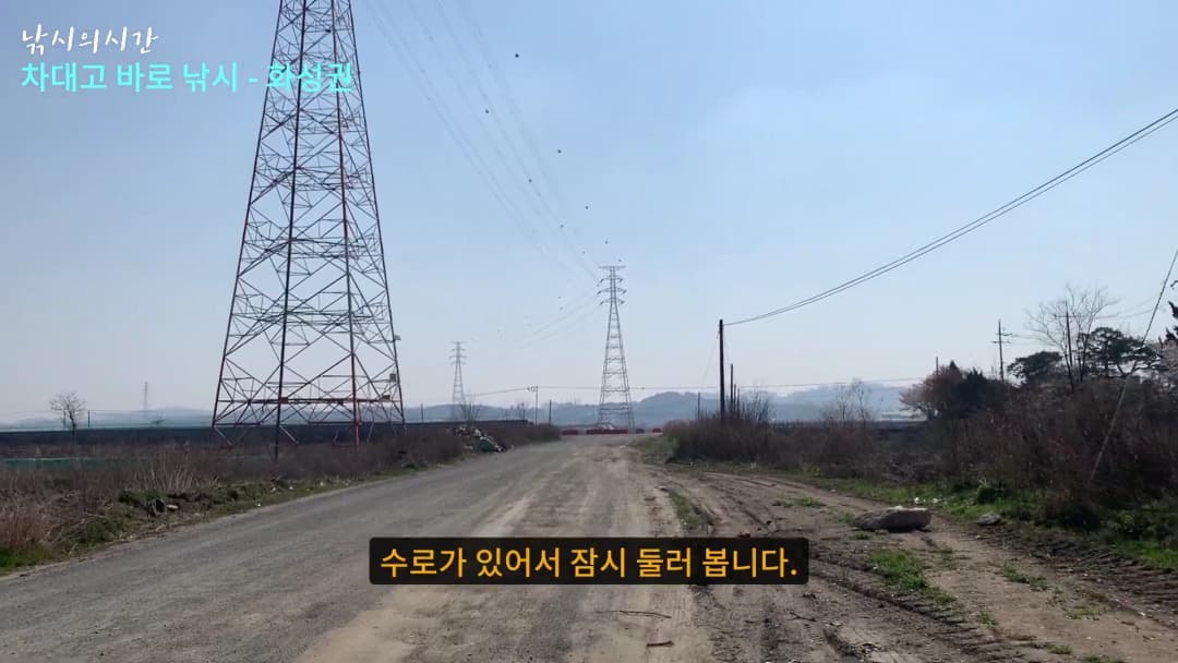 거대한 송전탑이 세워진 비포장도로와 주변 수로의 풍경